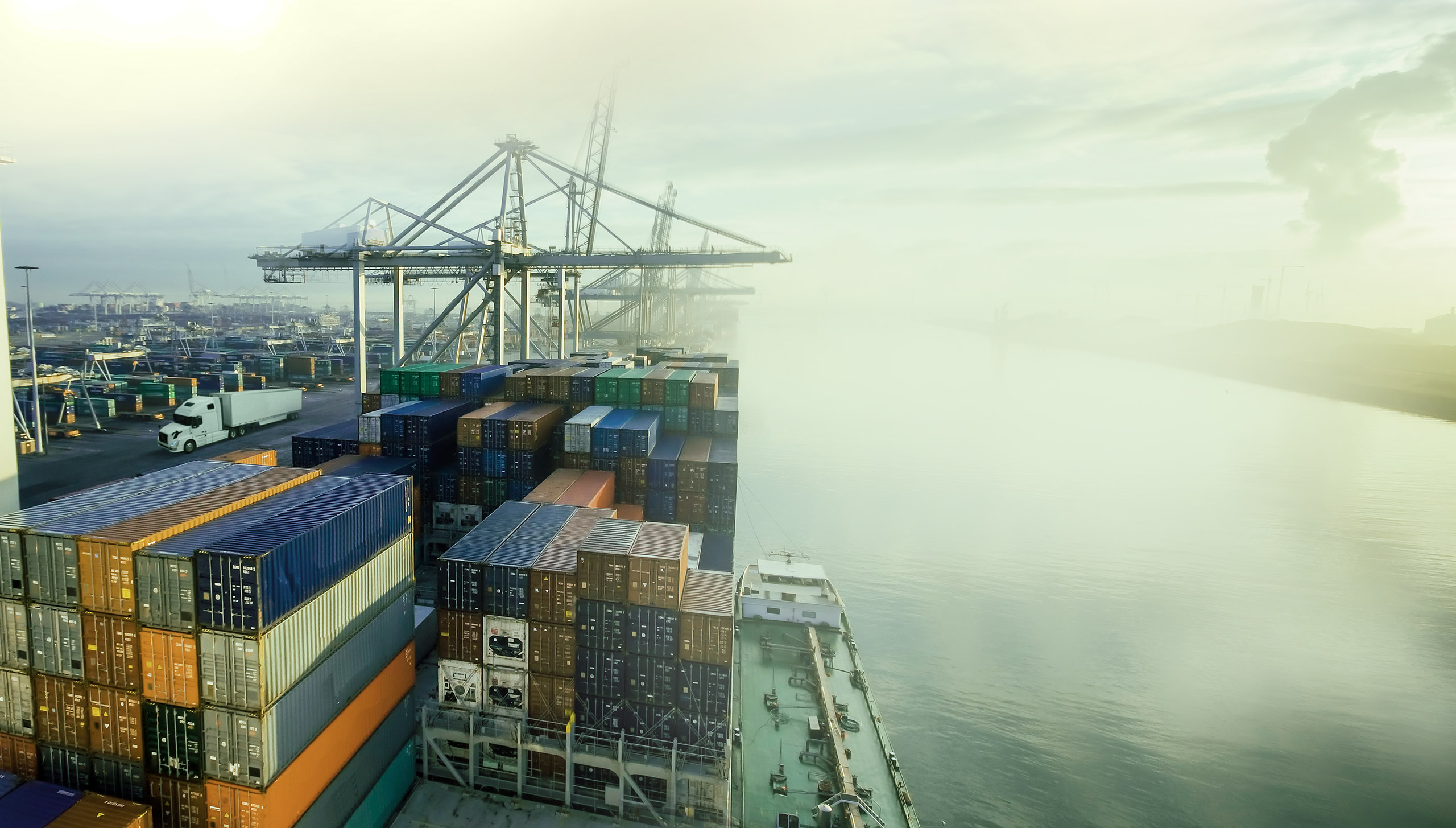 An ocean port with cargo ships, freight containers, cranes and a transport truck