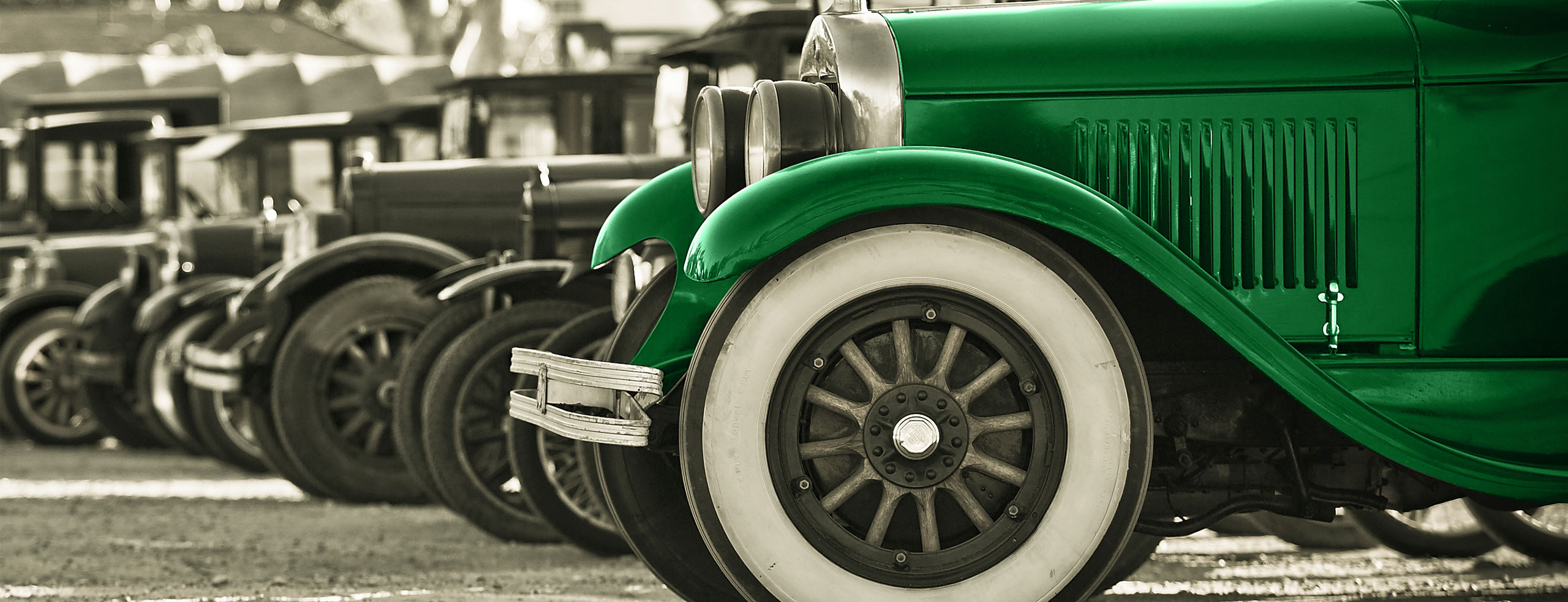 A black and white photo of a lineup of classic cars, with the first one in green
