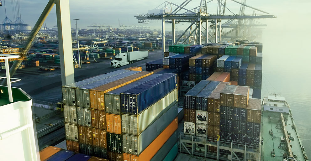 An ocean port with cargo ships, freight containers, cranes and a transport truck